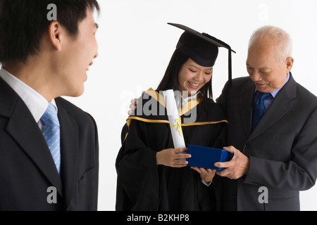 Junge weibliche Absolventin erhält ein Geschenk von ihrem Vater und lächelnd Stockfoto