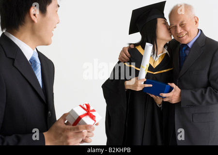 Junge weibliche Absolventin erhält ein Geschenk und küssen, ihr Vater und ein junger Mann hält ein Geschenk Stockfoto