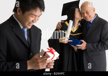 Junge weibliche Absolventin erhält ein Geschenk und küssen, ihr Vater und ein junger Mann hält ein Geschenk Stockfoto