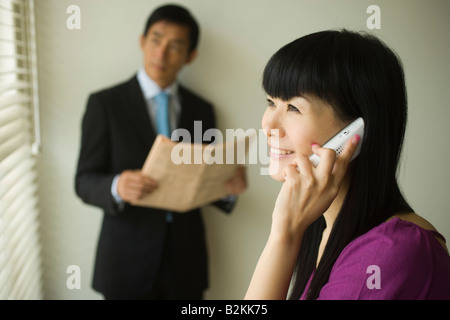 Nahaufnahme einer Geschäftsfrau Gespräch auf ein Mobiltelefon mit einem Geschäftsmann im Hintergrund Stockfoto