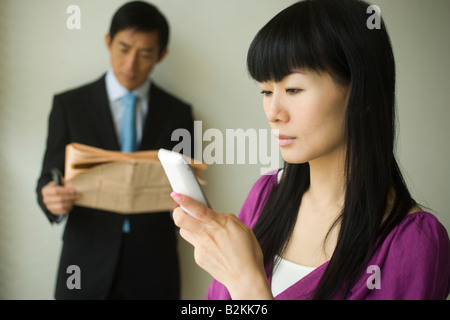 Nahaufnahme einer Geschäftsfrau hält ein Mobiltelefon mit einem Geschäftsmann im Hintergrund Stockfoto