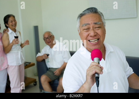 Nahaufnahme eines älteren Mannes in ein Mikrofon mit seinen Freunden im Hintergrund singen Stockfoto