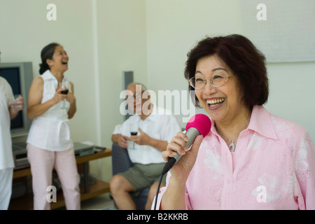 Nahaufnahme einer älteren Frau in Mikrofon mit ihren Freunden im Hintergrund singen Stockfoto