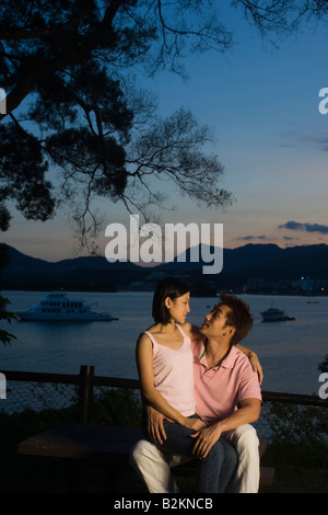 Mitte Erwachsene Frau sitzt auf dem Schoß eines jungen Mannes am Meer Stockfoto