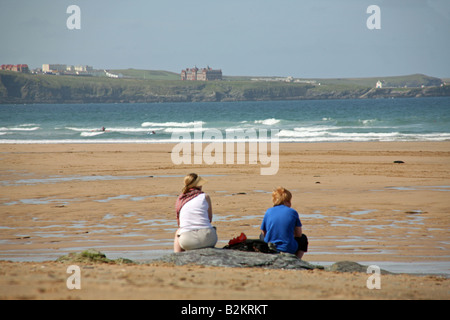 Ein paar Frauen entspannen am Strand, Blick auf das Meer bei Watergate Bay Strand, Newquay, Cornwall Stockfoto