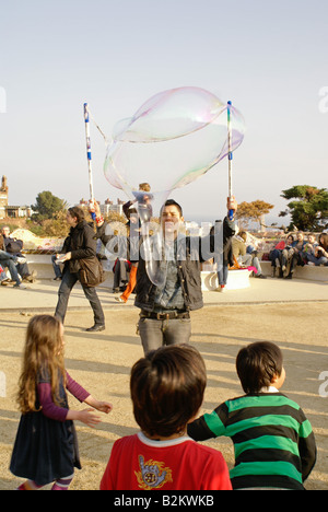 Kinder spielen mit Seifenblasen aus ein Straßenkünstler im Park Güell, Barcelona, Spanien Stockfoto