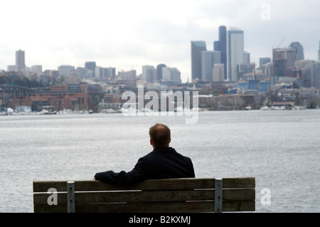 Ein Mann sitzt auf einer Bank mit Blick auf die Skyline von Seattle und Lake Washington. Stockfoto