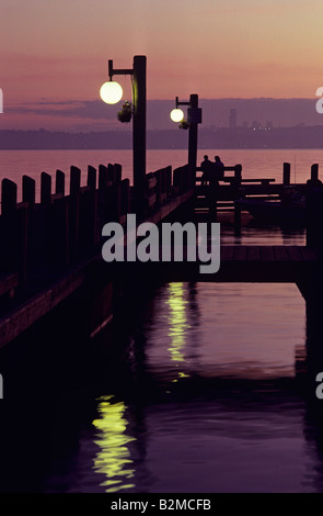 Silhouette paar auf Bank auf Dock am Lake Washington bei Sonnenuntergang mit Seattle Skyline im Hintergrund Kirkland Washington State Stockfoto