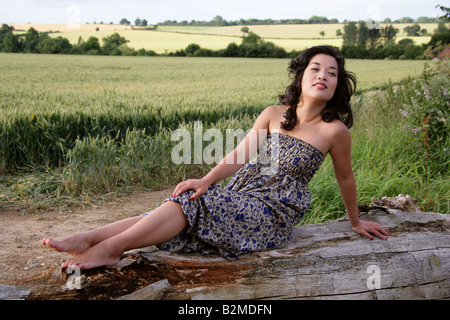 Chinesische Mädchen sitzen auf einem Baumstamm vor einem Maisfeld