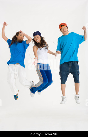 Zwei junge Frauen mit einem jungen Mann, anhören von MP3-Playern und springen Stockfoto