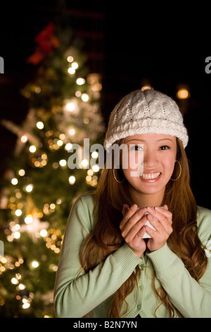 Nahaufnahme einer jungen Frau hält eine Tasse heiße Schokolade vor einem Weihnachtsbaum Stockfoto