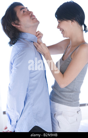 Junge Frau knöpfte das Hemd eines jungen Mannes und lächelnd Stockfoto