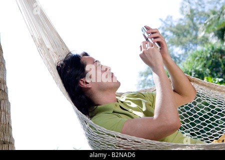 Junger Mann in einer Hängematte liegend und mit einem Palmtop, Phuket, Thailand Stockfoto