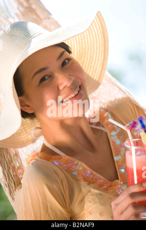 Porträt einer jungen Frau in einer Hängematte liegend und hält ein Glas Cocktail, Phuket, Thailand Stockfoto