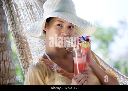 Porträt einer jungen Frau in einer Hängematte liegend und trinken cocktail, Phuket, Thailand Stockfoto