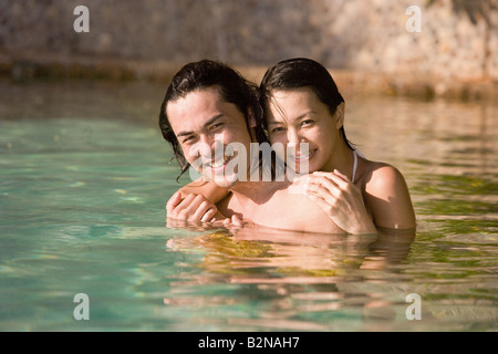 Porträt einer jungen Frau, die einen jungen Mann von hinten in einen Pool umarmen Stockfoto