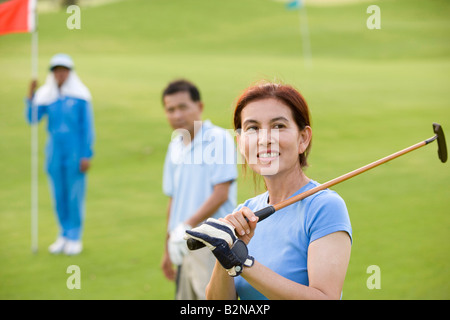 Reife Frau hält einen Golfclub mit zwei reife Männer stehen im Hintergrund Stockfoto