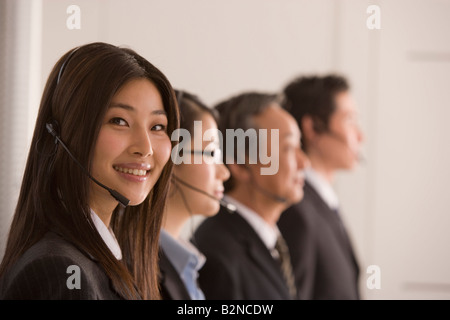 Porträt einer Geschäftsfrau trägt einen Kopfhörer und lächelnd mit drei Geschäftsleute neben ihr Stockfoto