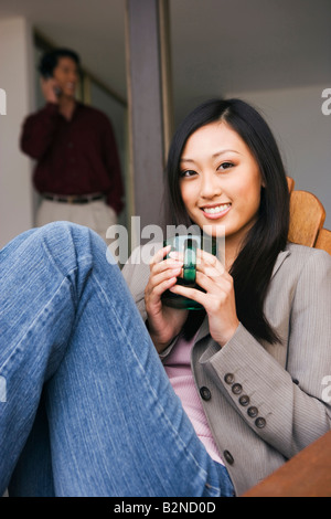 Porträt einer jungen Frau auf einem Stuhl sitzend und hält eine Tasse Kaffee Stockfoto