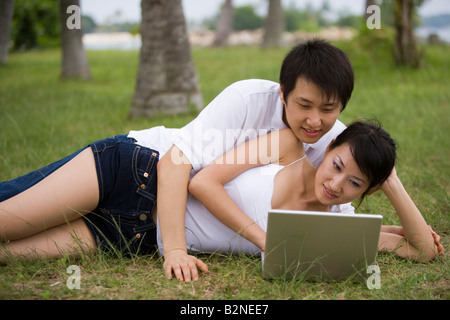 Junges Paar auf dem Rasen liegen und mit einem laptop Stockfoto