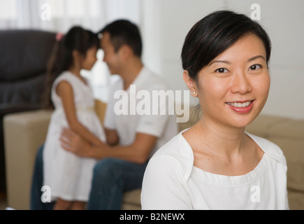 Porträt einer Mitte erwachsenen Frau lächelnd mit ihrer Tochter und der Mann im Hintergrund, Singapur Stockfoto