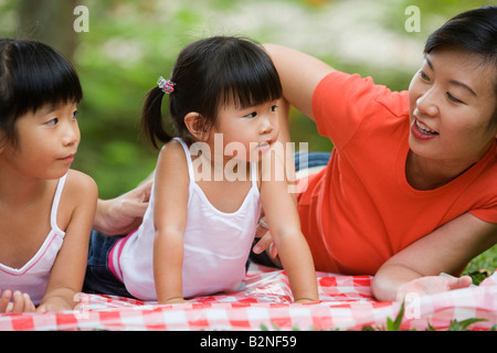 Mitte Erwachsene Frau liegend auf einer Picknickdecke mit ihren beiden Töchtern in einem Park, Singapur Stockfoto