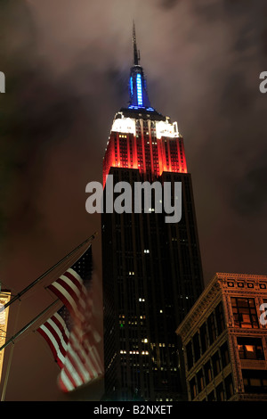 Empire State building in New York City in der Nacht mit amerikanischen Flaggen im Vordergrund rot weiße und blaue Lichter Stockfoto