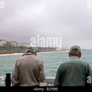 Zwei Menschen stehen auf Brighton Pier in West Sussex an einem windigen Tag bewölkt. Stockfoto