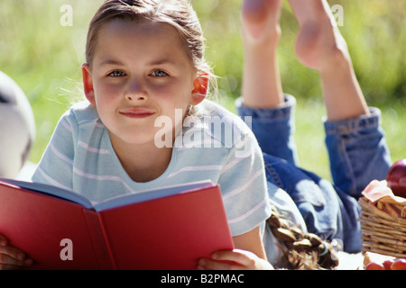 Ein junges Mädchen liest ein Buch, das sich bei einem Picknick im Sommer auf einer Decke legt Stockfoto