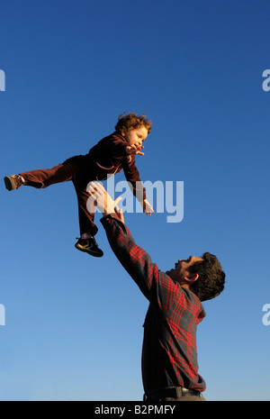 Ein fröhliches zwei Jahres altes Mädchen geworfen in den blauen Himmel von ihrem Vater vertikale Hochformat Stockfoto