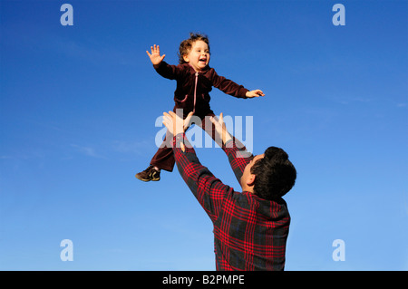 Ein glücklich zwei Jahre altes Mädchen von ihrem Vater in den blauen Himmel geworfen Stockfoto