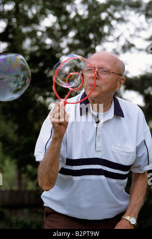 Älterer Mann bläst Seifenblasen im Hinterhof Stockfoto