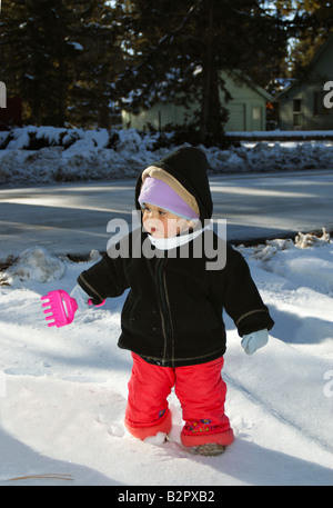 Ein Kleinkind Mädchen mit einem Spielzeug-Rechen stehen im Schnee Stockfoto