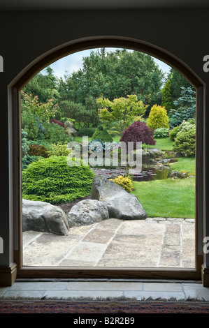 Blick aus dem Fenster in den Garten mit Terrasse, Teich, Sträucher & Bäume im Garten-Design von Bahaa Seedhom North Yorkshire England UK Stockfoto