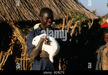 Behinderte Landwirt, die Kaninchen in den Armen, Angola, Afrika Stockfoto