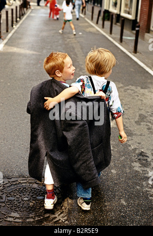 zwei Kinder teilen sich eine Erwachsenen-Größe Jacke in einer Umarmung Stockfoto