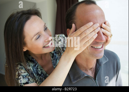 Lächelnde Frau ihres Mannes Augen versteckt Stockfoto