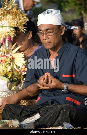 Bali Indonesien Kuta Strand Mann beten Feuerbestattung Zeremonie hindu religiösen Menschen sammeln Blumen Weihrauch brennen mit display Stockfoto