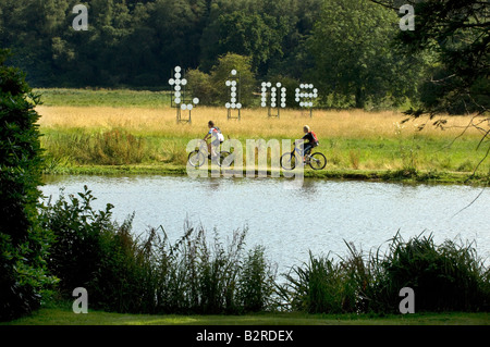 Zwei junge Radfahrer Talfahrt Ufer eines Flusses vorbei Bildhauer Jonathan Parsons Installation des riesigen schwimmenden Punktmatrix Buchstaben Zeit Stockfoto