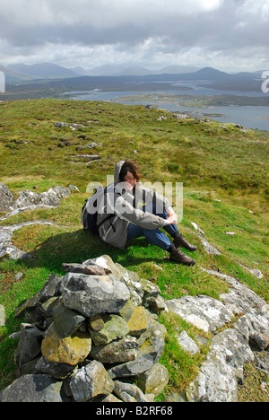 Frau an der Spitze des Mount Errisbeg, Roundstone, Connemara, County Galway, Irland mit der Twelve Bens in der Ferne. Stockfoto