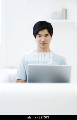 Junger Mann, sitzend mit Laptop, lächelnd in die Kamera Stockfoto