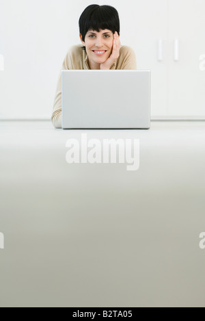 Frau liegend auf Bauch, lächelnd über Laptop in die Kamera, niedrigen Winkel Ansicht Stockfoto