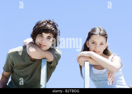 Bruder und Schwester seitwärts sitzen auf Stühlen, stützte sich auf Ellenbogen, lächelnd in die Kamera Stockfoto