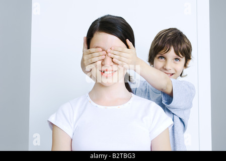 Bruder von seinen Schwestern Augen mit seinen Händen, Lächeln Stockfoto