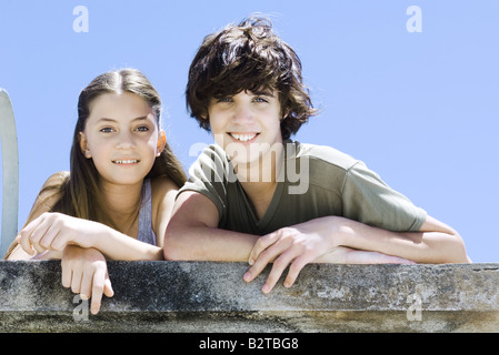 Bruder und Schwester nebeneinander, stützte sich auf Betonwand, lächelnd in die Kamera, Porträt Stockfoto