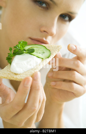 Junge Frau hält Cracker, garniert mit Gurken und Streichkäse, beschnitten Stockfoto