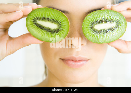 Frau mit Kiwi Hälften vor ihren Augen, Lächeln, Kopfschuss Stockfoto