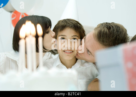 Familie hinter Geburtstagskuchen mit brennenden Kerzen, Eltern, junge auf Wangen küssen Stockfoto