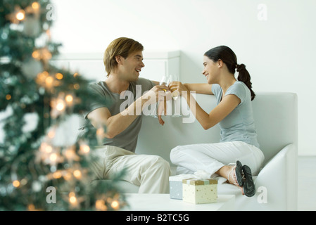 Paar macht einen Toast mit Champagner, Weihnachtsbaum im Vordergrund Stockfoto
