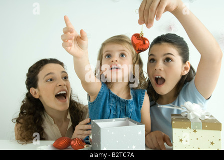 Mädchen Eröffnung präsentiert, eine Holding-Ornament, andere Strecken sich, Mutter beobachten Stockfoto